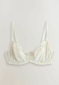 Soutien-gorge crème transparent avec armatures et petite broderie de marguerite blanche, bretelles réglables, posé à plat sur un fond clair.