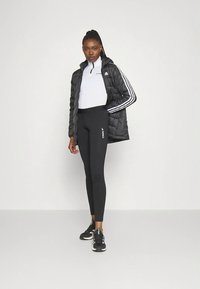 Μαύρο επενδυμένο μπουφάν με λευκές ρίγες, λευκή μπλούζα με φερμουάρ, μαύρο κολάν με λογότυπο και μαύρα αθλητικά παπούτσια. Απλός στυλ αθλητικής ένδυσης.