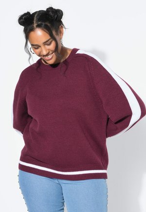 Bordeaux gebreide trui met witte strepen op de mouwen en de zoom. Ronde halslijn en een losse pasvorm, gecombineerd met lichtblauwe denim jeans.