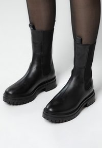 Stivali alla caviglia in pelle nera con finitura liscia, pannelli elastici laterali, linguette di presa e suola in gomma robusta. Design elegante e aderente.