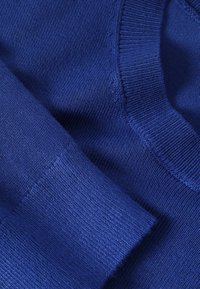 Gros plan sur un tissu tricoté bleu montrant les détails côtelés des poignets et du col d’un pull.