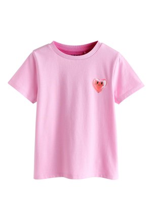 T-shirt rosa in cotone a maniche corte con un piccolo cuore lucido raffigurante un volto sorridente sul lato sinistro del petto.