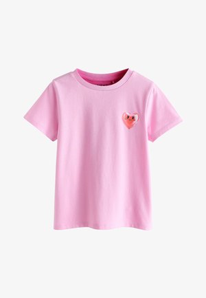 Roza majica kratkih rukava od pamuka s malim sjajnim srcem koje ima nasmiješeno lice na lijevoj prsa.