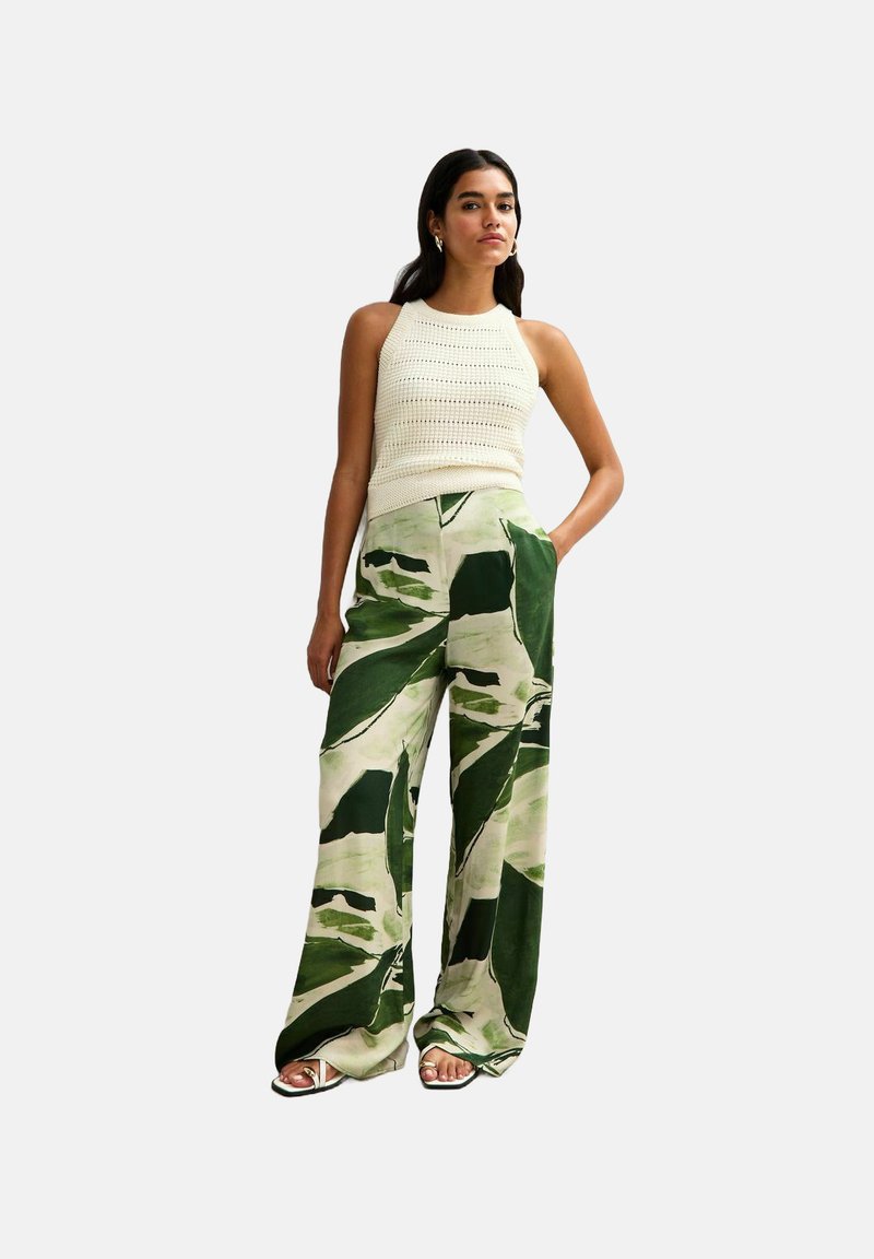 Witte gebreide haltertop gecombineerd met wijde broek met een groen en crèmekleurig bladenpatroon, gemaakt van lichte stof.