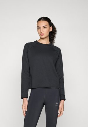 Black ribbed long-sleeve sweatshirt with a crew neckline, relaxed fit, and visible stitching. Paired with dark leggings featuring logo detail.