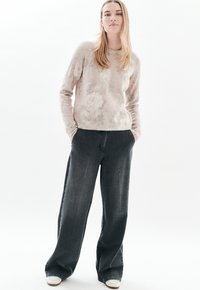 Vaaleanpunainen kukkakuosiset neule, jossa on pitkät hihat, yhdistettynä tummiin leveisiin farkkuihin ja valkoisiin lenkkareihin, seisoo valkoista taustaa vasten.