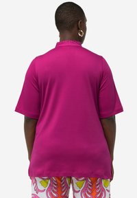 Fuchsia relaxte blouse met korte mouwen, voorzien van een hoge halslijn en versieringen, gemaakt van soepele stof, gecombineerd met een gebloemde broek.