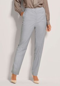 Lichtgrijze broeken van zachte stof, met een rechte pasvorm en zijzakken. Gecombineerd met een glanzende bruine blouse en beige hakken.