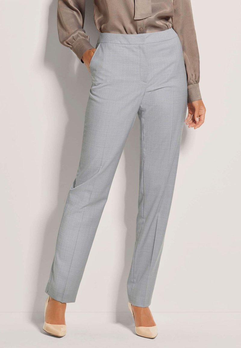 Lichtgrijze broeken van zachte stof, met een rechte pasvorm en zijzakken. Gecombineerd met een glanzende bruine blouse en beige hakken.