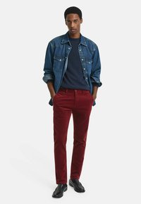 Denim overhemd met twee borstzakken, marineblauwe trui en rode corduroy broek, gecombineerd met zwarte instappers.