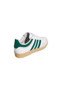 Witte lage sneaker met groene strepen, groene hielstik, beige zool en vetersluiting, gezien vanuit een achterzijaanzicht.