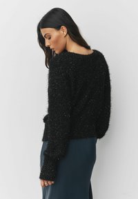 Black fluffy sweater in a textured knit, featuring long sleeves and a wide neckline. Paired with a dark blue satin skirt.