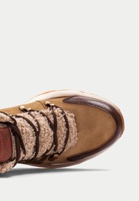 Botín de ante marrón con detalles de cuero marrón, tejido beige texturizado y cordones marrones. Presenta ojales de metal y una suela de goma blanca.