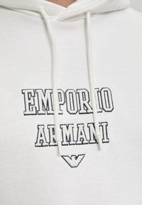 Felpa bianca con cappuccio e cordino. Logo ricamato nero "EMPORIO ARMANI" sul petto. Tessuto morbido, vestibilità casual, senza fantasie.