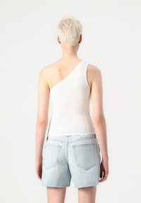 Hvit, en-skulder tank topp laget av glatt stoff, kombinert med lyseblå denimshorts med baklommer og opprevet nederkant.