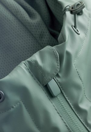 Nepremokavá bunda z jemného, ľahkého materiálu v mätovo zelenej farbe; má hladkú textúru, nastaviteľné šnúrky a zosilnené švy.