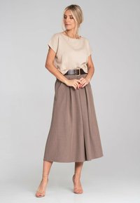 Beżowa bluzka z krótkim rękawem o luźnym kroju, zestawiona z brązową plisowaną spódnicą midi oraz szerokim brązowym paskiem. Przezroczyste paski na sandałach.