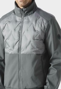 Szary płaszcz z pikowaną górną częścią w diamentowy wzór, gładką dolną częścią, zamek błyskawiczny i boczne kieszenie.