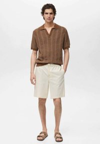 Bruin gestreept poloshirt met korte mouwen en kraag, gecombineerd met crèmekleurige shorts en bruine sliders. Relaxte pasvorm en textuurstof.