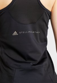 Svart atletisk linne med nätpaneler, en fitted design och logodetaljer i silver. Mjuk textur med förstärkt sömnad.