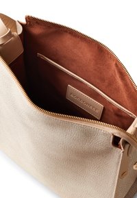 Borsa in pelle beige con esterno testurizzato, zip dorata e interno in suede marrone con tasca a sottoposizione e etichetta del marchio.
