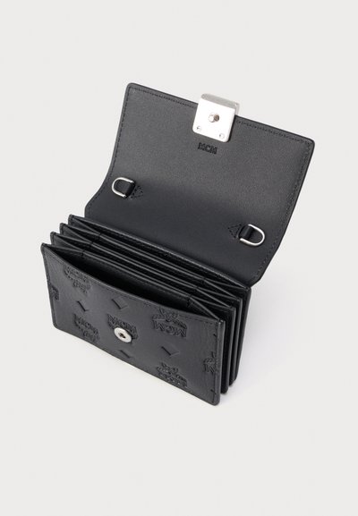 Μαύρο δερμάτινο πορτοφόλι MCM ανοιχτό, που εμφανίζει πολλαπλές θήκες για κάρτες, ασημένιο κούμπωμα με κουμπί και ανάγλυφο μοτίβο λογότυπου στο εξωτερικό μέρος.