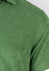 Polo verde realizzato in tessuto texturizzato. Presenta un colletto e maniche corte. Aspetto liscio e morbido con una distribuzione uniforme del colore.