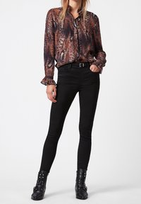 Long-sleeve, multicolored blouse with animal print, button front, and ruffled cuffs, paired with black skinny jeans and black ankle boots.