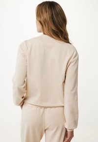 Svetle béžová mikina s dlouhými rukávy, kulatým výstřihem, uvolněným střihem a hladkou strukturou, doplněná o odpovídající kalhoty.