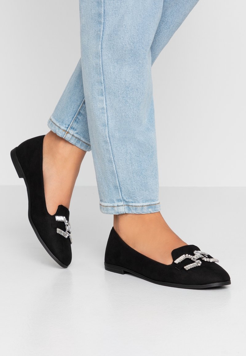 Ballerines en daim noir à texture lisse, ornées de strass à l'avant. Le design est élégant avec un petit talon.
