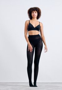 Schwarzer BH und hochgeschnittene schwarze Leggings aus weichem, dehnbarem Material mit dezenten Glitzerakzenten überall. Das Model steht vor einem hellen Hintergrund.