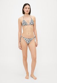 Svartvit blommig bikini-set bestående av en triangeltopp och nederdel med knytband, tillverkad av ett slätt tyg med en åtsittande design.