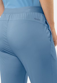 Hellblaue Sporthose mit glatter Textur, elastischem Bund und kleinem Logo in der Nähe des Bundes. Figurbetontes Design mit seitlichen Taschen.