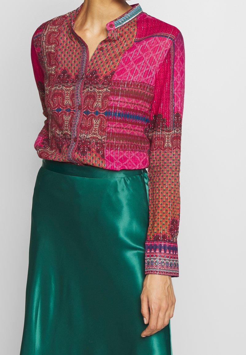Rosa gemusterte Bluse mit Knopfleiste, präsentiert mit unterschiedlichen Texturen und lebhaften Farben, kombiniert mit einem glatten grünen Satinrock.