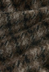 Brūnas un melnas rakstainas vilnas audums ar mīkstu, teksturētu virsmu, kurā redzami šķiedras un viļņota forma.