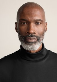 Sort rullekrave i glat stof med høj krave. Personen har kortklippet hår og fuld grå skæg.