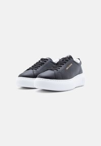 Μαύρα δερμάτινα αθλητικά παπούτσια με παχιά λευκά πέλματα, μαύρα κορδόνια και χρυσό λογότυπο «Armani Exchange» στο πλάι.