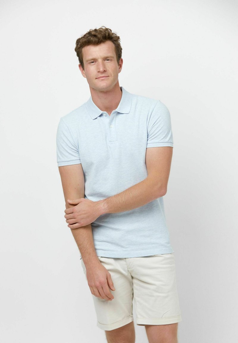 Polo azul claro hecho de algodón suave, de manga corta, con cuello abotonado, combinado con pantalones cortos beige remangados.