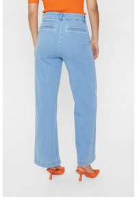 Gaiši zila, plaša kāju džinsu bikses ar aizmugurējām kabatām un tīriem apakšmalām. Pāris ar oranžu augstpapēžu apavu un pieguļošu oranžu topu.