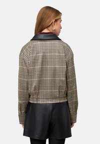 Korte jas met een zwarte leren kraag, voorzien van een ruitpatroon in beige en zwart. Soepele textuur met een losse pasvorm.