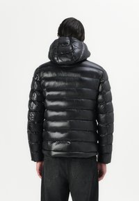 Schwarze Bomberjacke mit glänzender Oberfläche, horizontalem Steppmuster und Kapuze. Verfügt über elastische Bündchen und eine taillierte Silhouette.