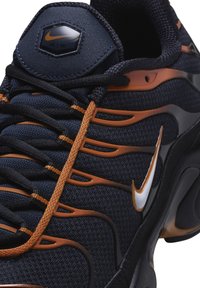 Baskets Nike Air avec un dessus en mesh bleu marine agrémenté d'accents orange et de motifs latéraux, des lacets noirs et un logo hexagonal sur la languette.
