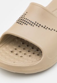 Bezs színű, nyitott orrú csúszó szandál, texturált talppal, fekete pöttyös részletekkel a felsőrészen a design gazdagítására.