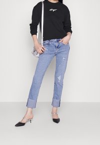 Felpa nera con logo, jeans chiari strappati con risvolti, e mules nere appuntite con fascia argentata.