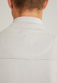 Hellegrauer Strickpullover mit hohem Kragen, der über ein dezentes gesticktes Logo und eine strukturierte Rippung am Kragen und an den Nähten verfügt.