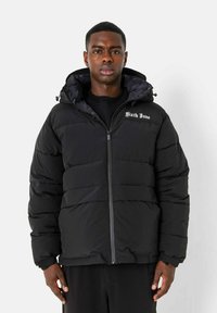 Zwarte pufferjas met een ritssluiting aan de voorkant, capuchon en geborduurd "Sixth June" logo op de borst. Kenmerkt zich door een matte afwerking en een gestikte uitstraling.