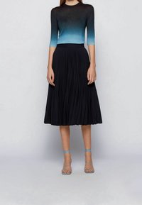 Pletený top s gradientem od černé k modré, spárovaný s černou plisovanou midi sukní a světle modrými sandály na tenkých řemíncích.