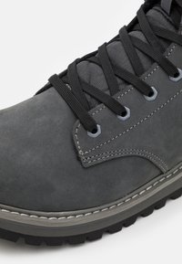 Chaussure en cuir gris foncé avec une finition texturée, dotée de lacets noirs, de coutures contrastantes et d'une semelle en caoutchouc noir robuste.