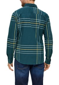 Groen geruiten overhemd met gele en witte lijnen, voorzien van lange mouwen en een gebogen zoom. Gecombineerd met blauwe spijkerbroeken.