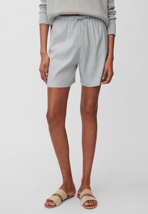 Shorts gris clair avec une taille à cordon, présentant une coupe décontractée et une texture lisse. Associés à des sandales à glisser beiges.